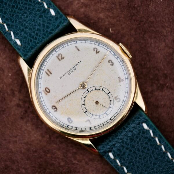 The 1940s Vacheron Constantin Caltrava V453 is a timeless vintage wristwatch featuring a gold case, subtly worn white dial with Arabic numerals, and a subdial at the 6 oclock position. The black leather strap with white stitching enhances its classic look, while the brand name stands proudly on the dial.