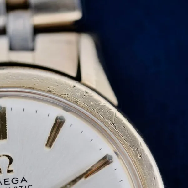 Close-up of a vintage Omega Seamaster L6298 Dauphine Hands wristwatch featuring a metallic case with visible scratches. The cream-colored dial has dark hour markers and partial text reading MEGA and MATIC, exuding a classic, polished design.