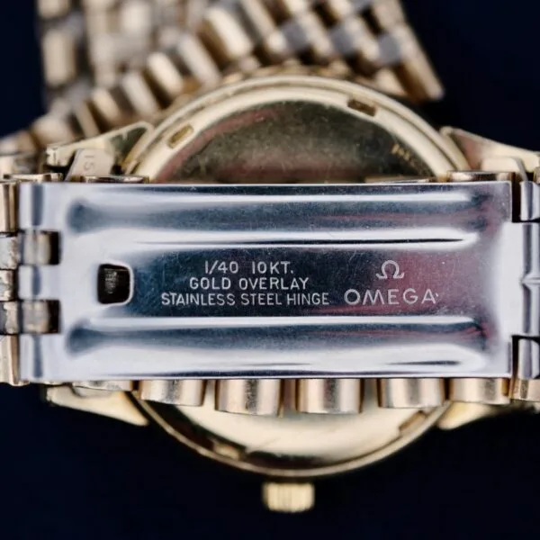 A close-up image captures the vintage allure of an Omega Seamaster L6298 Dauphine Hands wristwatchs metal clasp, featuring 1/40 10KT. GOLD OVERLAY STAINLESS STEEL HINGE OMEGA, emphasizing its metallic charm and gold finish.