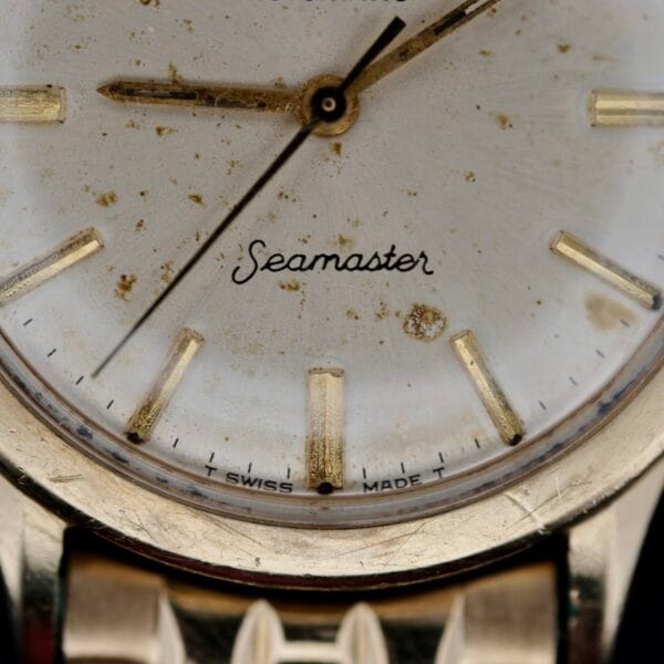 A close-up reveals Seamaster elegantly in cursive on the vintage Omega Seamaster L6298 Automatic watch face. The dial, with signs of wear, features gold hour markers and hands on a silver background. At the bottom, T SWISS MADE T is inscribed, marking its timeless craft.