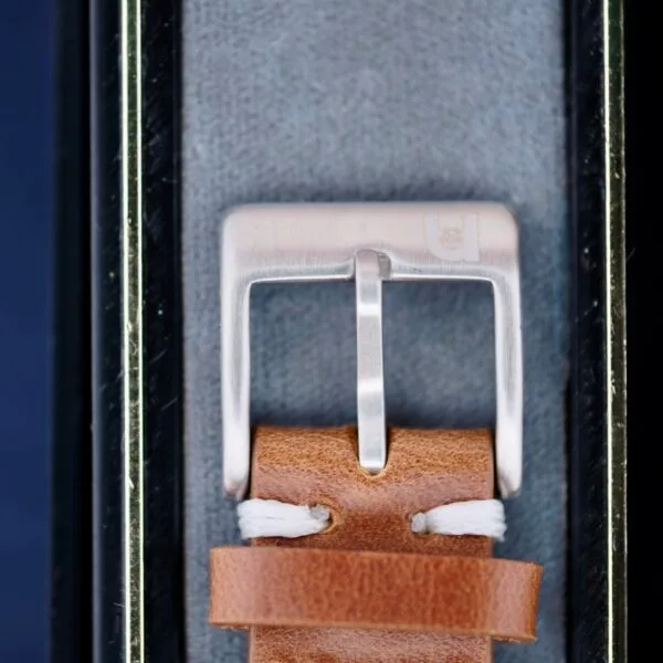 The Omega Ref 14713 Bark Dial watchs silver buckle and brown leather strap with white stitching exude vintage charm. Nestled in a gray velvet-lined case, the smooth-finished buckle and elegant design capture timeless elegance.