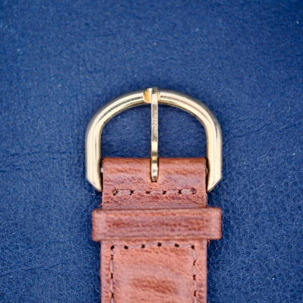 Close-up of a 1950s Hamilton Automatic with a brown leather strap and gold buckle against a dark blue textured background.