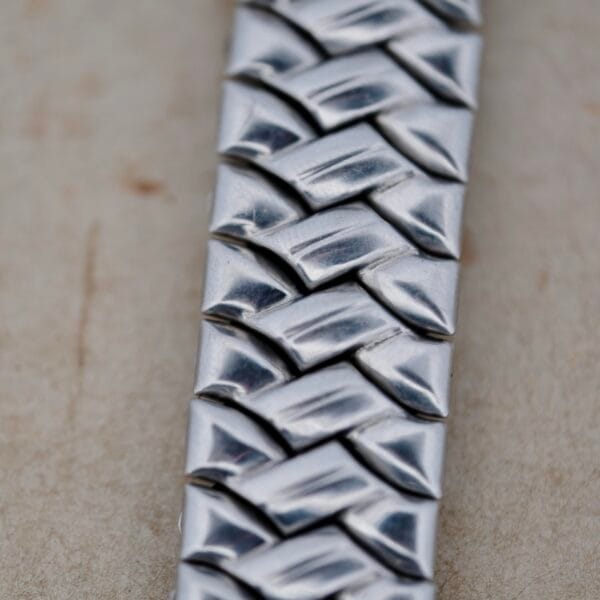 Close-up of the Benrus Triple Calendar in Steel, showcasing its reflective silver metal surface with a herringbone pattern. The intricate design is highlighted against a neutral, blurred background.