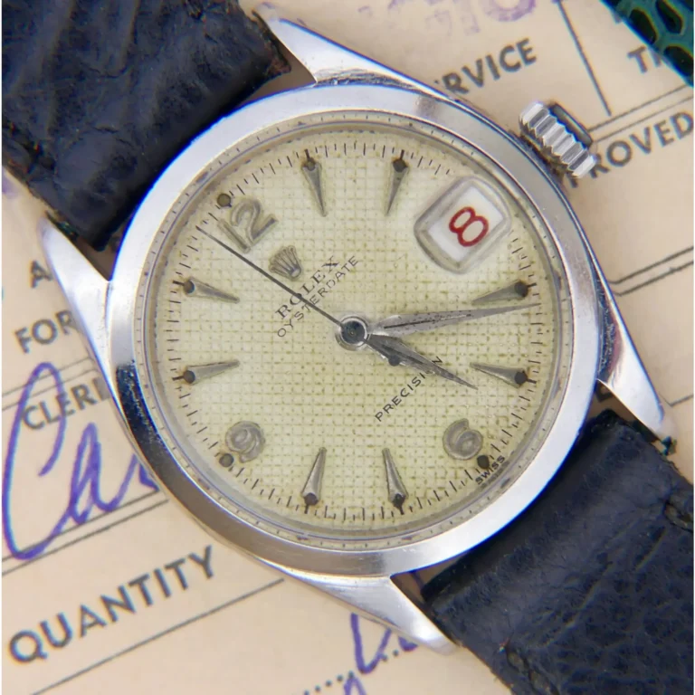 A 1953 Rolex Oyster Date 6266 with a cream textured dial, black leather strap, silver case, and date display at 8, shown resting atop paperwork.