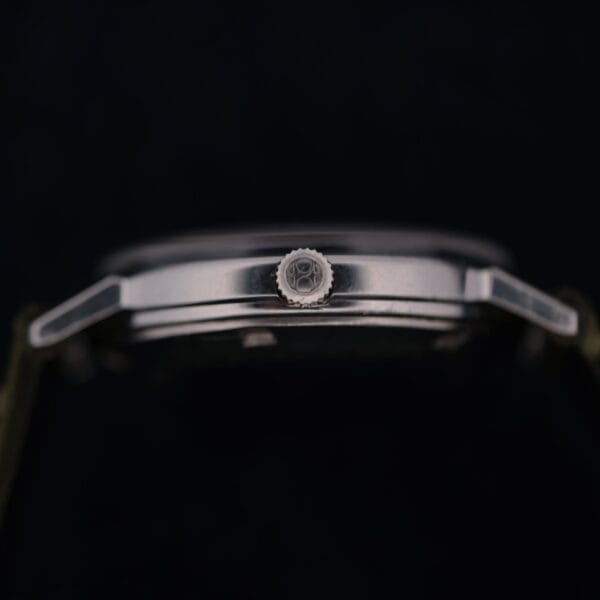Side view of the 1960 Hamilton Thin-o-Matic T-501 Micro-Rotor in a dark setting, highlighting its metal case, lugs, and gear-patterned crown.