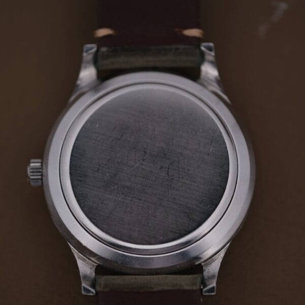 A close-up of the back of a 1960s IWC Automatic Dress Watch Cal. 853 with a leather strap, displaying its plain silver case back with minor scratches; the crown is visible on the left side.