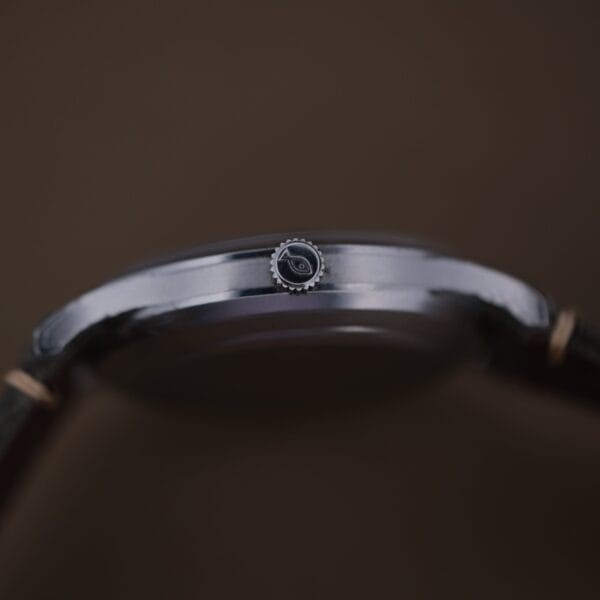 A close-up side view of the 1960s IWC Automatic Dress Watch Cal. 853 shows its thin metal case, black crown, and leather strap against a plain dark background.