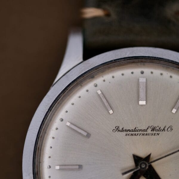 Close-up of a 1960s IWC Automatic Dress Watch Cal. 853, showing the silver face with International Watch Co. Schaffhausen, metal bezel, silver hour markers, and part of the strap visible at the top.