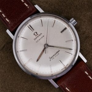 A 1963 Omega Seamaster Deville Türler Dial Ref. 135.010 wristwatch with a brown leather strap rests on a dark textured surface.