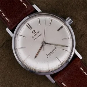 A 1963 Omega Seamaster Deville Türler Dial Ref. 135.010 wristwatch with a brown leather strap rests on a dark textured surface.