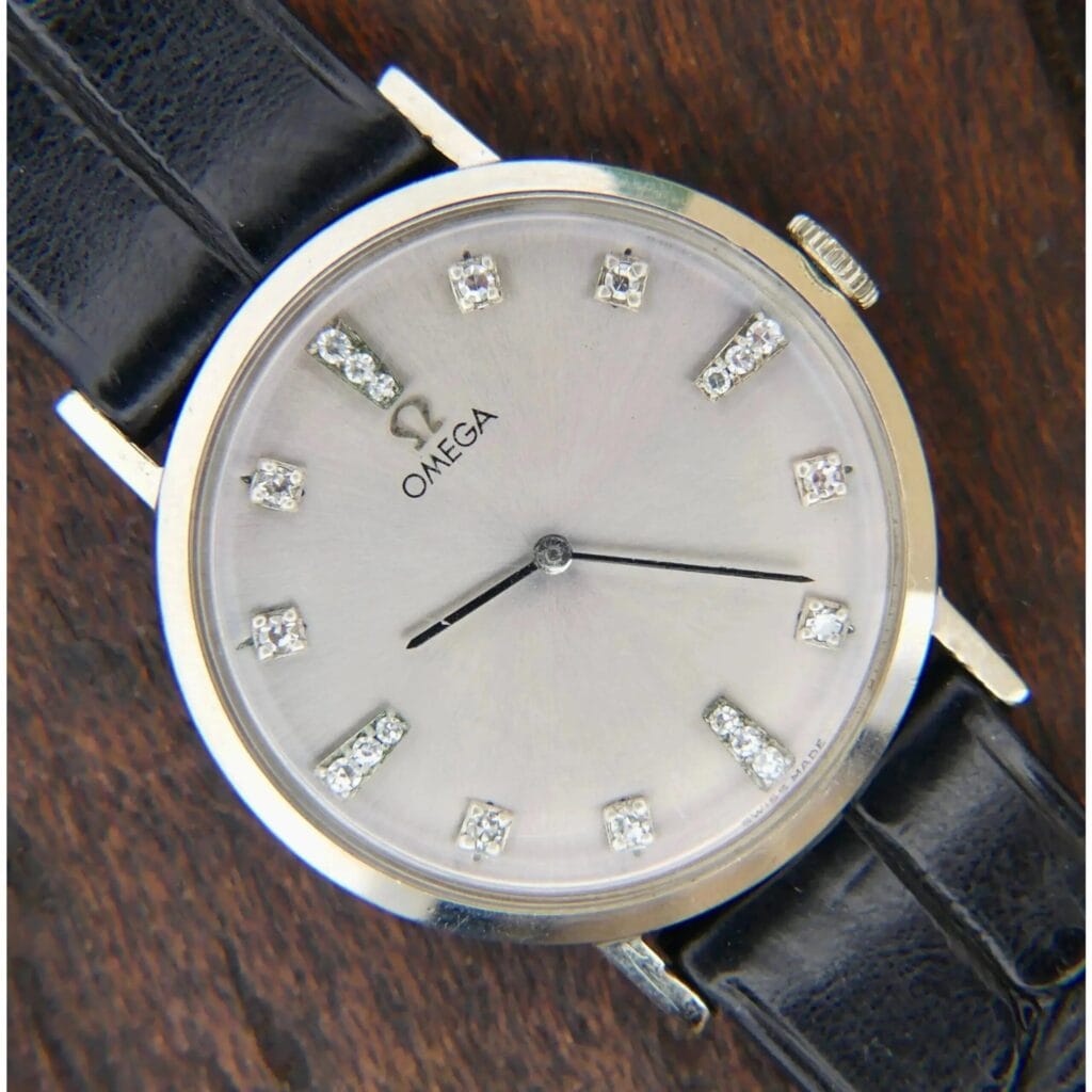 1965 Omega Deville Ref. D6672 wristwatch with 14k gold and diamond markers, black leather strap, displayed on a wooden surface.