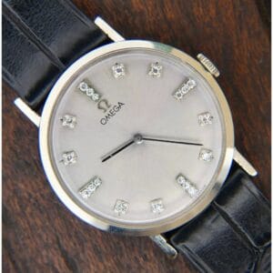 1965 Omega Deville Ref. D6672 wristwatch with 14k gold and diamond markers, black leather strap, displayed on a wooden surface.