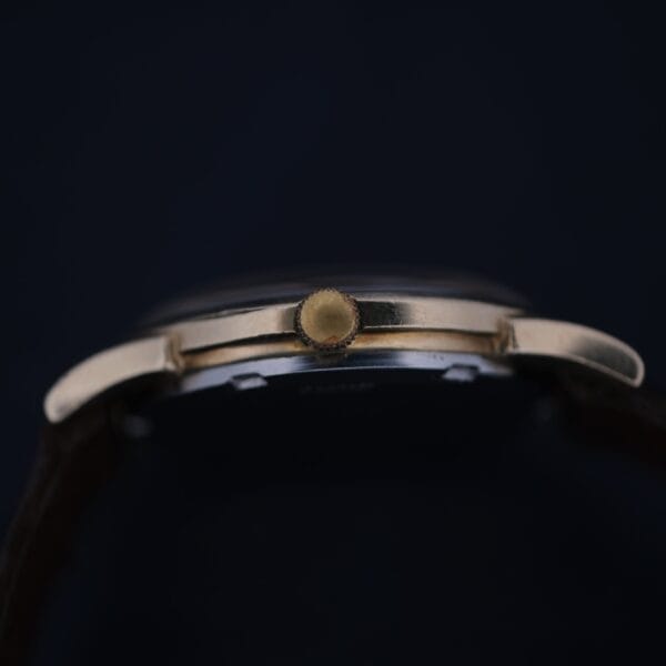 Close-up side view of the crown on a 1966 Omega Automatic Date Cal. 563 wristwatch against a black background, highlighting part of the gold case and the winding stem.
