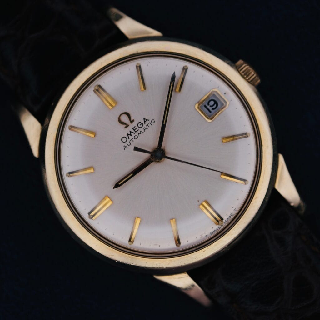 1966 Omega Automatic Date Cal. 563 wristwatch featuring a white dial, black leather strap, and date displayed as the 19th.