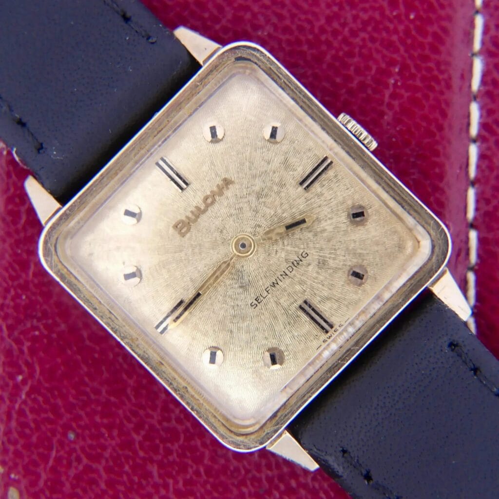 1968 BULOVA Automatic ‘Edwardian’ vintage square dress watch with black leather strap, displayed on a red textured background.