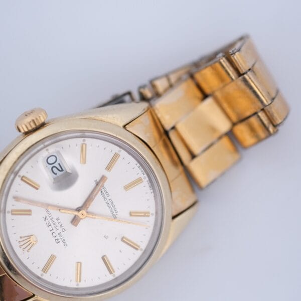 The 1974 Rolex Oyster Perpetual Date Ref. 1550, featuring a 14k gold shell wristwatch with a metallic band, shows a date window indicating the 20th and has gold hour markers. The slightly worn hands and band suggest vintage or regular use.