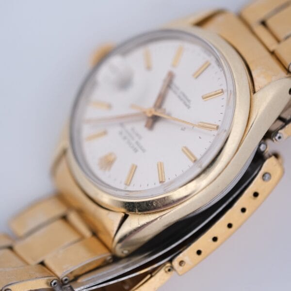 Close-up of a 1974 Rolex Oyster Perpetual Date Ref. 1550 14k Gold Shell wristwatch with a white dial, gold hour markers, three hands, and a date display. The angled view showcases its gold-finish metal band and part of the clasp.