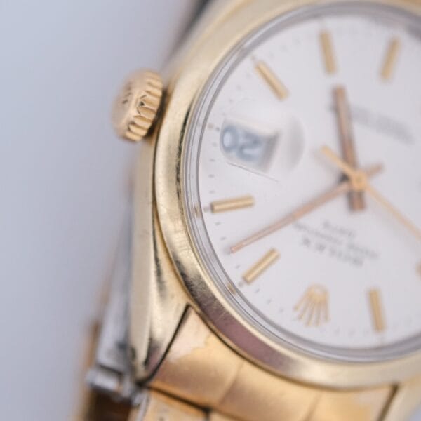 Close-up of a 1974 Rolex Oyster Perpetual Date Ref. 1550 featuring a gold shell, white dial, gold hour markers and hands, fluted bezel, date window, crown on the left side, and part of the bracelet visible at the bottom.