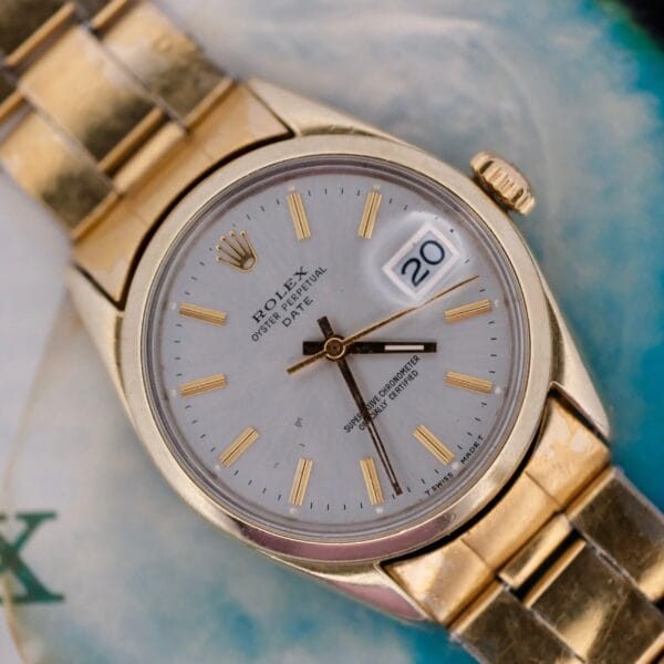 Close-up of a 1974 Rolex Oyster Perpetual Date Ref. 1550 in 14k gold with a white face, gold hour markers, and the date set to 20. The blurred background highlights the branding Rolex and Oyster Perpetual on the dial.