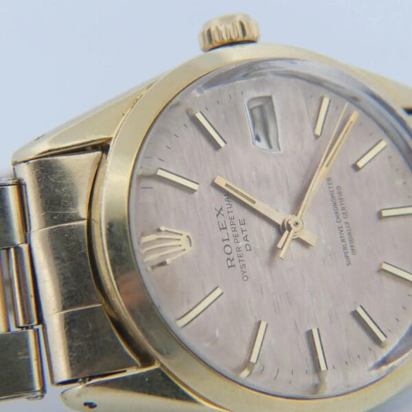 Close-up of a 1978 Rolex 1550 Oyster Perpetual Date in 14k gold shell with a white face. It showcases the brand name, has gold hour markers and hands, features a date window, and includes a gold linked bracelet.