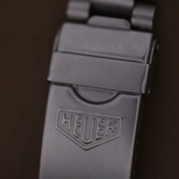 Close-up of the matte metal clasp on a 1986 Tag Heuer 2000 Series Blue Bezel Ref. 972.606 1st Gen, featuring the embossed HEUER logo against a dark background and showing slight signs of wear.