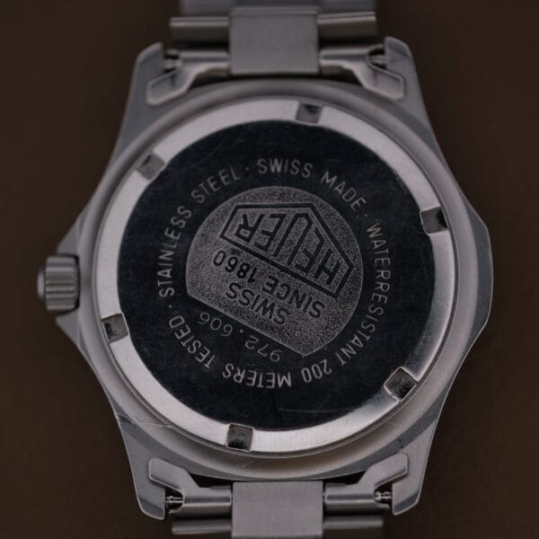 A close-up of the back of a stainless steel 1986 Tag Heuer 2000 Series Blue Bezel Ref. 972.606 1st Gen wristwatch, showing engraved details like the logo, Swiss Made, Since 1860, and water resistance specs.