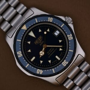 Close-up of a 1986 Tag Heuer 2000 Series Blue Bezel Ref. 972.606 1st Gen wristwatch with metal band, featuring a blue bezel and dial, resting on a brown surface.