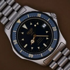 Close-up of a 1986 Tag Heuer 2000 Series Blue Bezel Ref. 972.606 1st Gen wristwatch with metal band, featuring a blue bezel and dial, resting on a brown surface.