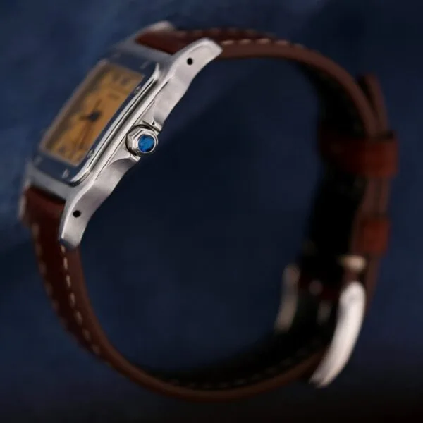 A close-up side view of the 1990s Cartier Santos Galbée ref. 1564 wristwatch with a rectangular silver case, brown leather strap, and a blue gemstone on the crown, set against a dark blue background.