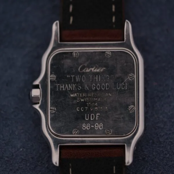 A close-up of the back of a 1990s Cartier Santos Galbée ref. 1564 with a brown leather strap. The engraving reads: “‘TWO THINGS. THANKS & GOOD LUCK!’ WATER RESISTANT SWISS MADE 1504 CC7964 UDF 86-96.”.