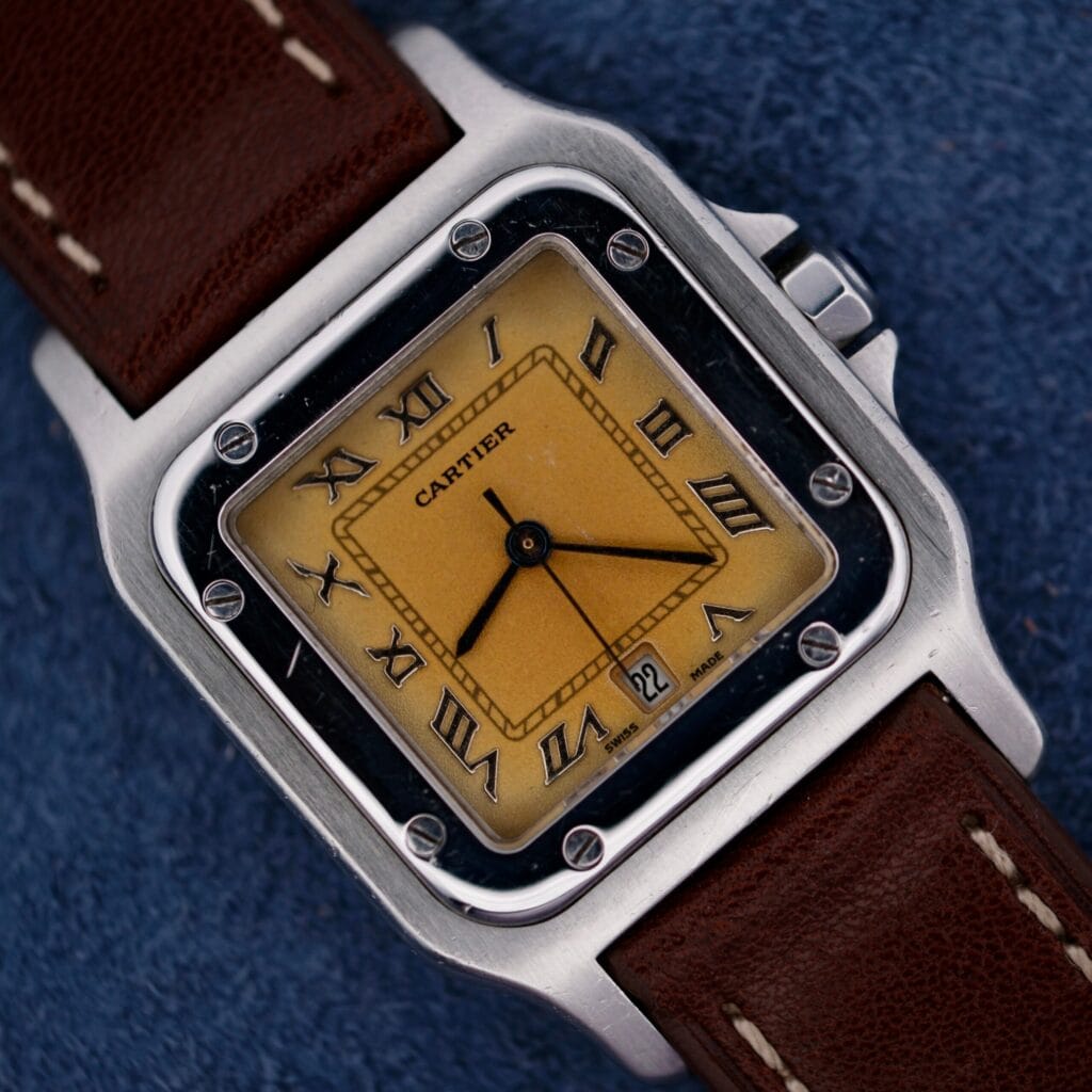 1990s Cartier Santos Galbée ref. 1564 with a yellow dial, Roman numerals, and a brown leather strap displayed on a blue fabric background.