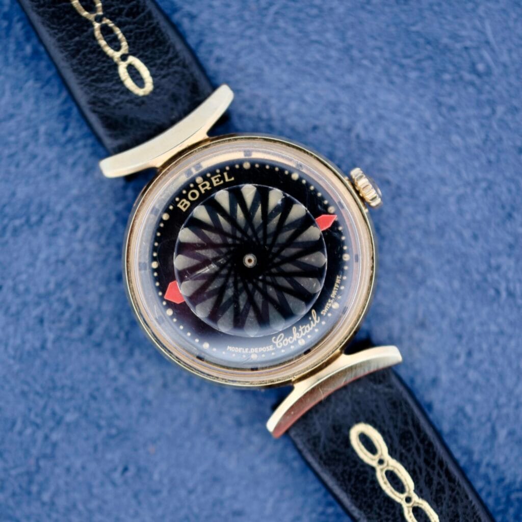 The Ernest Borel Kaleidoscope Cocktail Black Dial watch features a bold black dial and black leather strap, presented against a blue background.