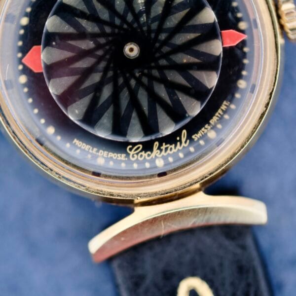 Close-up of the Ernest Borel Kaleidoscope Cocktail Black Dial watch with a captivating black and white pattern. The gold case is paired with a blue leather strap, while Cocktail, Modele Depose, and Swiss Patent are elegantly marked on the dial.