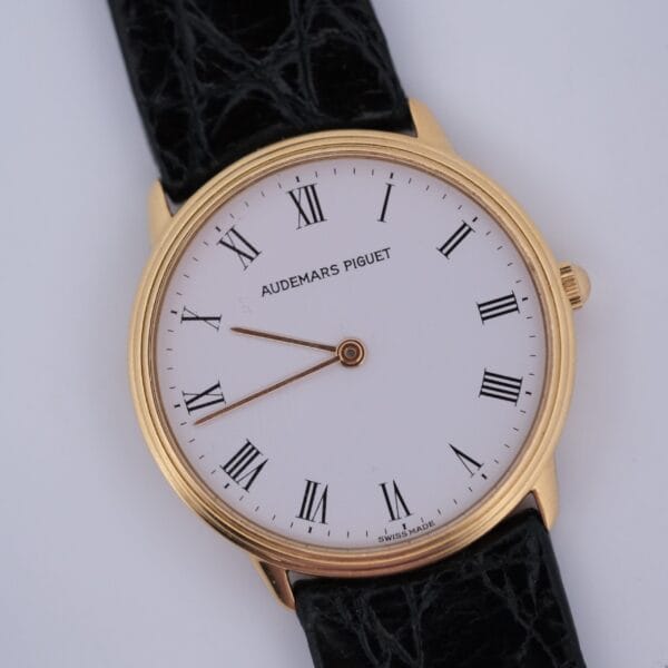 The Audemars Piguet Classic 18k Gold Roman Numerals watch features a white dial with black Roman numeral markers, a black leather strap, and displays the time at about 10:10:35.