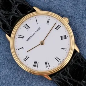 Audemars Piguet Classic 18k Gold Roman Numerals watch with a black leather strap, shown on a blue textured surface.