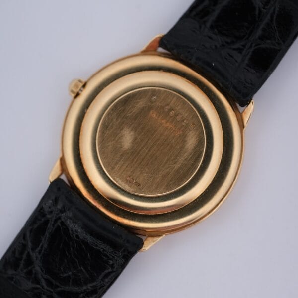 A close-up of the back of the Audemars Piguet Classic 18k Gold Roman Numerals wristwatch, featuring a round, smooth gold case with engraved markings and a black leather strap.