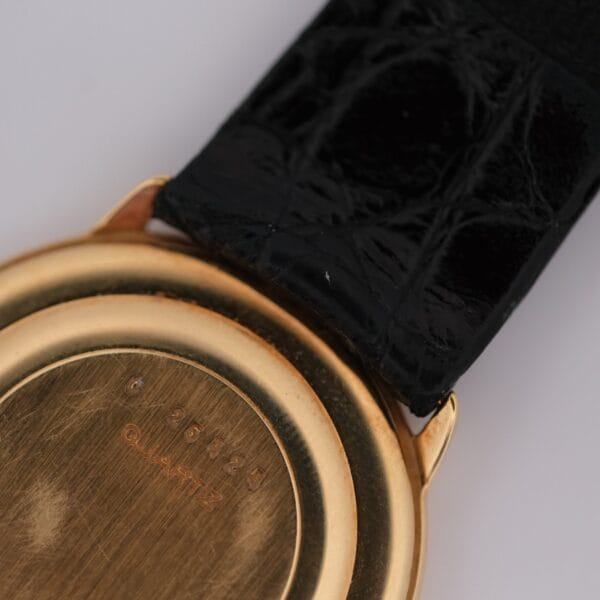 Close-up of the back of the Audemars Piguet Classic 18k Gold Roman Numerals watch with a black leather strap. QUARTZ and small engraved numbers appear on its metal case.