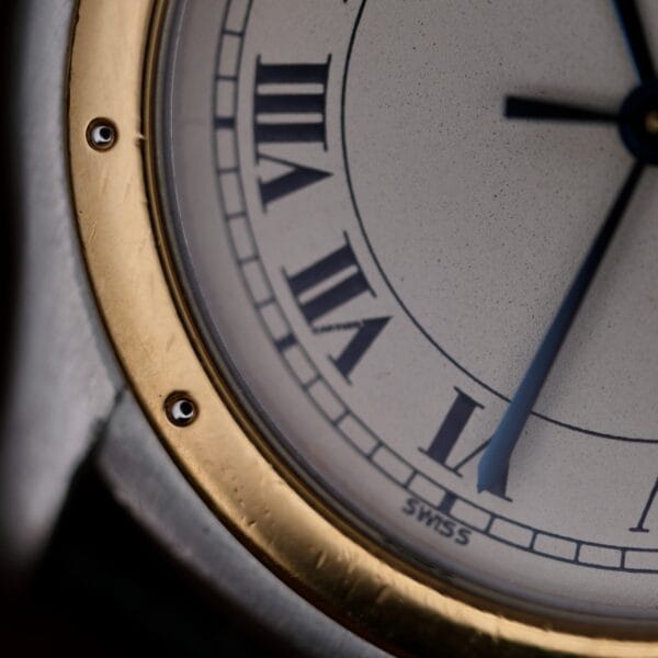 A close-up of the Cartier Cougar Gents Date Ref. 187904 watch face shows Roman numerals, a gold and silver bezel, blue hands displaying about 4:19, and SWISS at the bottom.