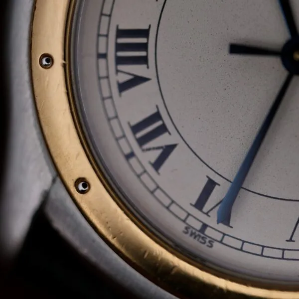 A close-up of the Cartier Cougar Gents Date Ref. 187904 watch face shows Roman numerals, a gold and silver bezel, blue hands displaying about 4:19, and SWISS at the bottom.