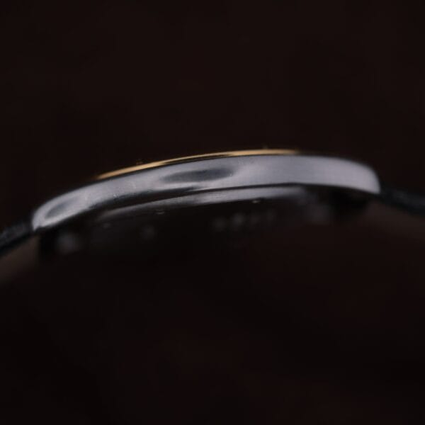 Close-up side profile of the Cartier Cougar Gents Date Ref. 187904 case against a dark background, highlighting its thin metal edge with subtle reflections and gently curved shape.