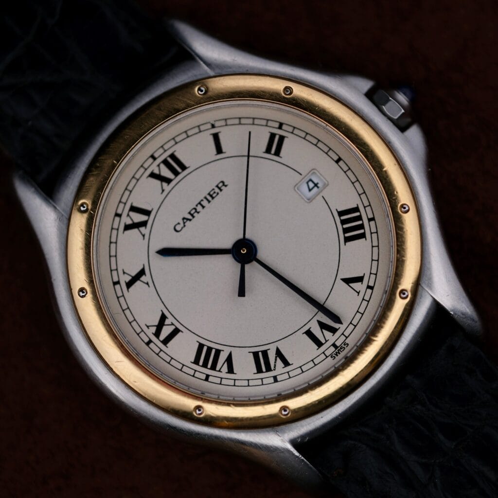 Cartier Cougar Gents Date Ref. 187904 wristwatch featuring classic Roman numerals, gold bezel, black leather strap, and date window positioned at 4 oclock.