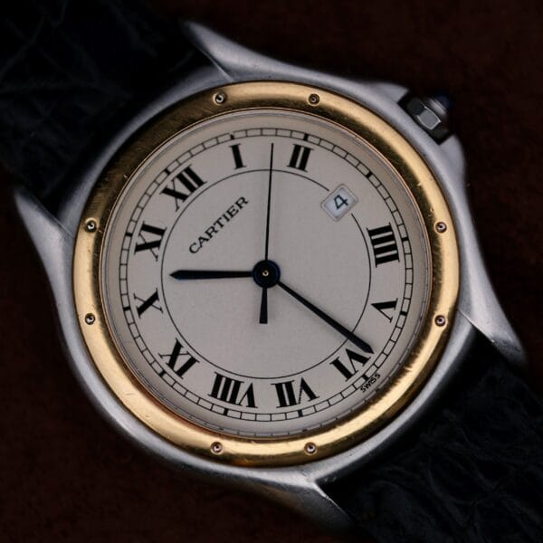 A close-up of the Cartier Cougar Gents Date Ref. 187904 wristwatch with a round white dial, black Roman numerals, gold bezel, black leather strap, and a date window showing 4. The time displayed is approximately 8:19:37.