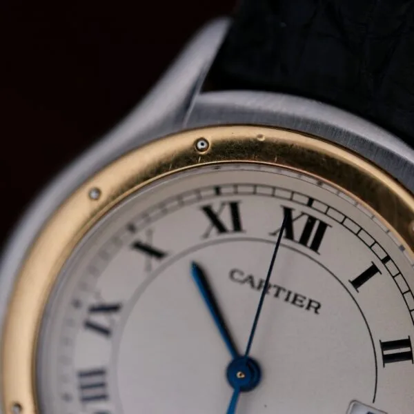 Close-up of a Cartier Cougar Gents Date Ref. 187904 wristwatch with Roman numerals, gold and silver bezel, blue hands, black leather strap, and the time showing approximately 12:56.