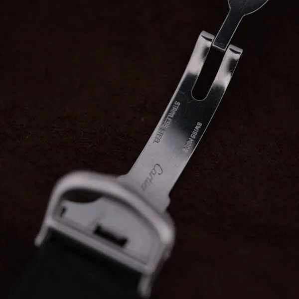 A close-up of the Cartier Cougar Gents Date Ref. 187904 stainless steel clasp with engraved markings, photographed against a dark brown textured background.