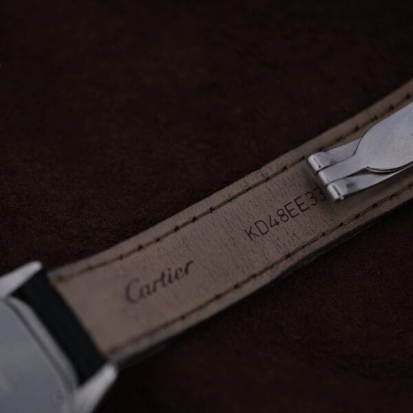 A close-up of a leather watch strap for the Cartier Cougar Gents Date Ref. 187904, with Cartier and the code KD48EE33 stamped underneath, displayed against a dark brown background.