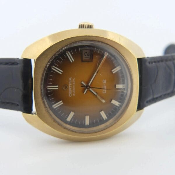 A vintage Certina DS-2 watch with a Gold Turtle case, black leather strap, and orange-brown ombre dial featuring white hour markers and a date display at the 3 oclock position.