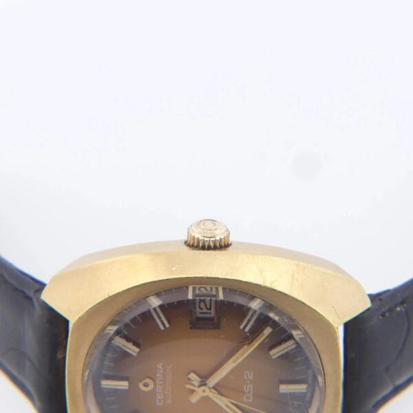 The Certina DS-2 features a gold-toned turtle case and an orange-brown ombre dial with silver hour markers, including a date window at 12 oclock. It is complemented by a black leather strap. Model: Cal. 25-651M.