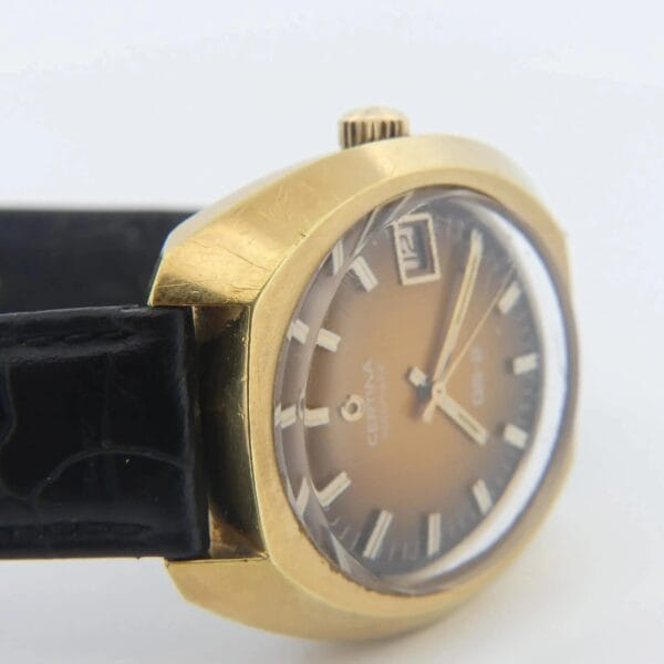 The Certina DS-2 watch features a gold-toned analog design with a round face, date window, baton hour markers, and an orange-brown ombre dial. It has a black crocodile-textured leather strap.