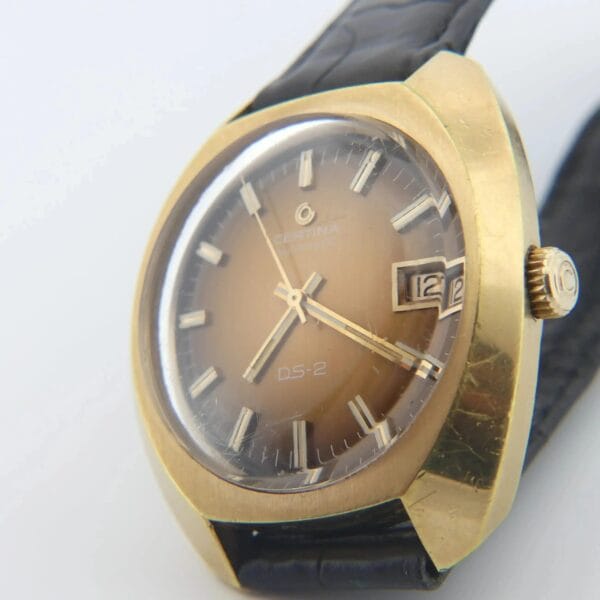 A vintage Certina DS-2 with a gold-turtle case, orange-brown ombre dial, black leather strap, silver hour markers, hands, a date window at 3 oclock, and right-side crown.