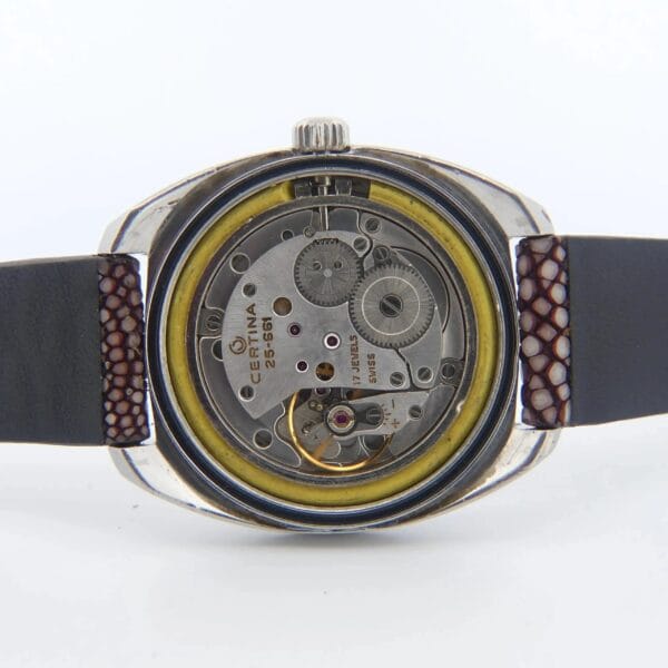 The image displays the open back of the Certina DS-2 Turtle Case Orange Second Black Dial Cal. 25-661, revealing its intricate mechanical movement. The metallic case features visible brand engraving, and the strap appears to be leather.